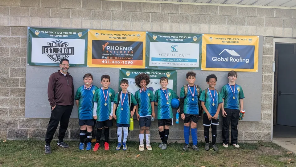 An NSYSA team and their coach standing beneath the sponsor banners at the field